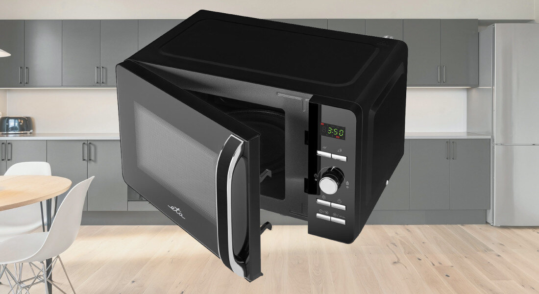 Kuchenka mikrofalowa ETA Gavento ETA120990010 Zdjęcie pokazuje urządzenie z otwartymi drzwiczkami na tle kuchni z szarymi szafkami i jasną podłogą. Mikrofalówka została sfotografowana pod lekkim kątem, co uwydatnia zarówno komorę, jak i panel sterowania blokada dzieci bezpieczne użytkowanie automatyczne wyłączenie wygodne otwieranie sygnał dźwiękowy intuicyjna obsługa