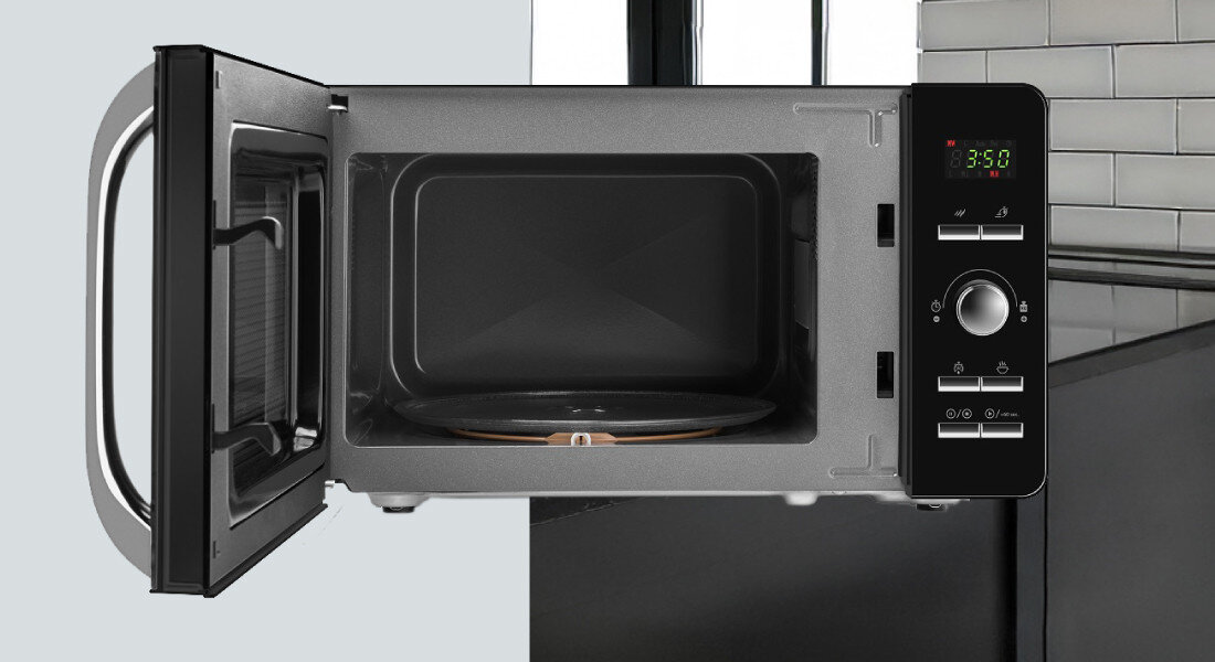 Kuchenka mikrofalowa ETA Gavento ETA120990010 Zdjęcie pokazuje mikrofalówkę z otwartymi drzwiczkami na tle kuchni z jasną ścianą i czarnym blatem. Widoczne jest wnętrze komory oraz wyświetlacz i przyciski po prawej stronie kompaktowy rozmiar 20 litrów talerz obrotowy czarny design oszczędność miejsca wygląd