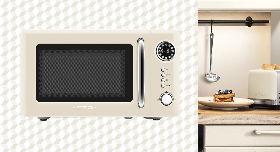 Beżowa kuchenka mikrofalowa z okrągłym panelem sterowania i przyciskami, z widocznym logo \'ETA\'. Obok znajduje się kuchnia z talerzem z jedzeniem i tosterem.