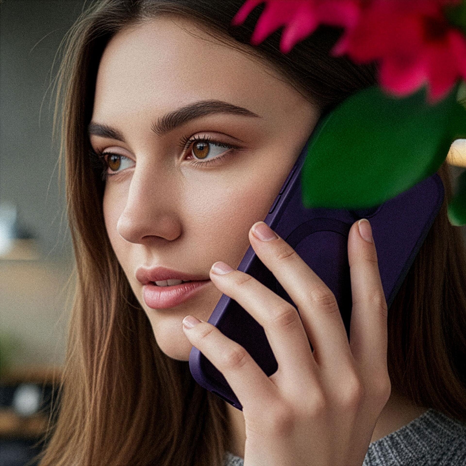 Osoba trzyma przy uchu telefon w fioletowym etui. W tle widoczne są rozmyte elementy wnętrza i zielone liście.