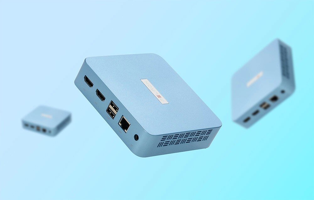 Komputer PELADN WI-6 Trzy jasnoniebieskie, niewielkie jednostki centralne o kwadratowym kształcie unoszą się w przestrzeni na jasnobłękitnym, rozmytym tle, prezentując tylne złącza komunikacyjne