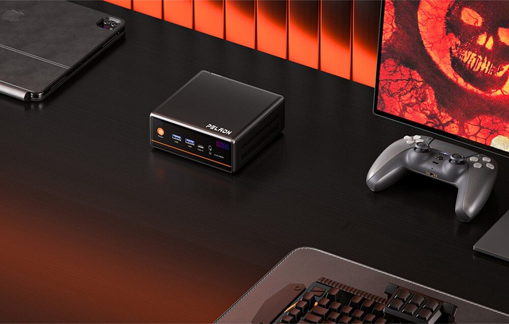 Komputer PELADN WO4 Mały komputer typu mini PC w czarnej obudowie z pomarańczowymi akcentami stoi na ciemnym biurku obok kontrolera do gier, klawiatury i monitora wyświetlającego grafikę z gry