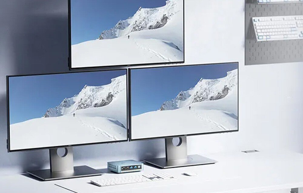 Komputer PELADN WI-6 N150 Stanowisko pracy z trzema monitorami wyświetlającymi ten sam krajobraz górski, podłączonymi do jednej małej jednostki centralnej leżącej na białym biurku