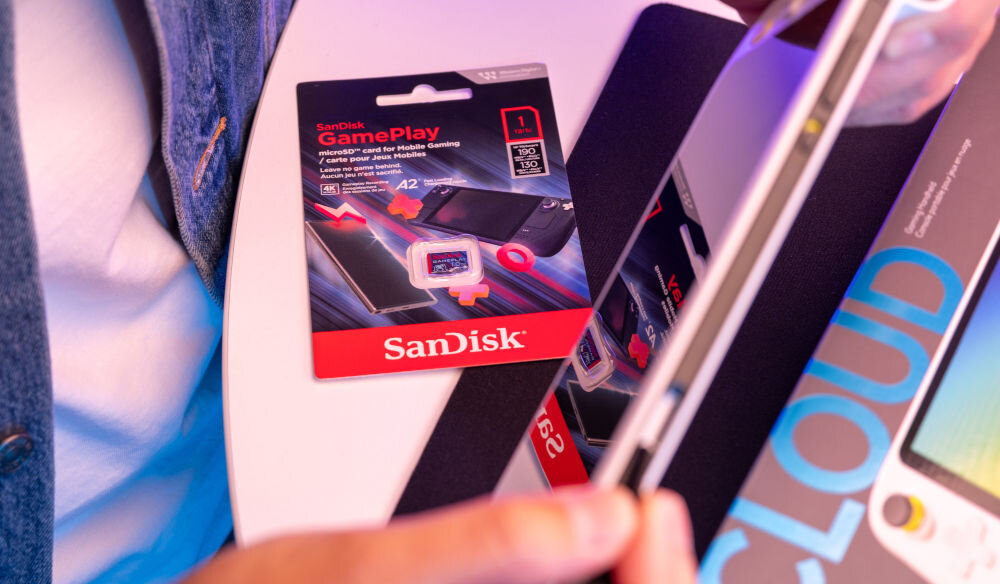 Karta pamięci SANDISK Gameplay MicroSDXC 1TB prezentacja prezentacja karty w opakowaniu mężczyzna trzymający konsolę w rękach w tle pudełko obsługa gier AAA i grafiki 3D VR stabilna rozgrywka bez spowolnień