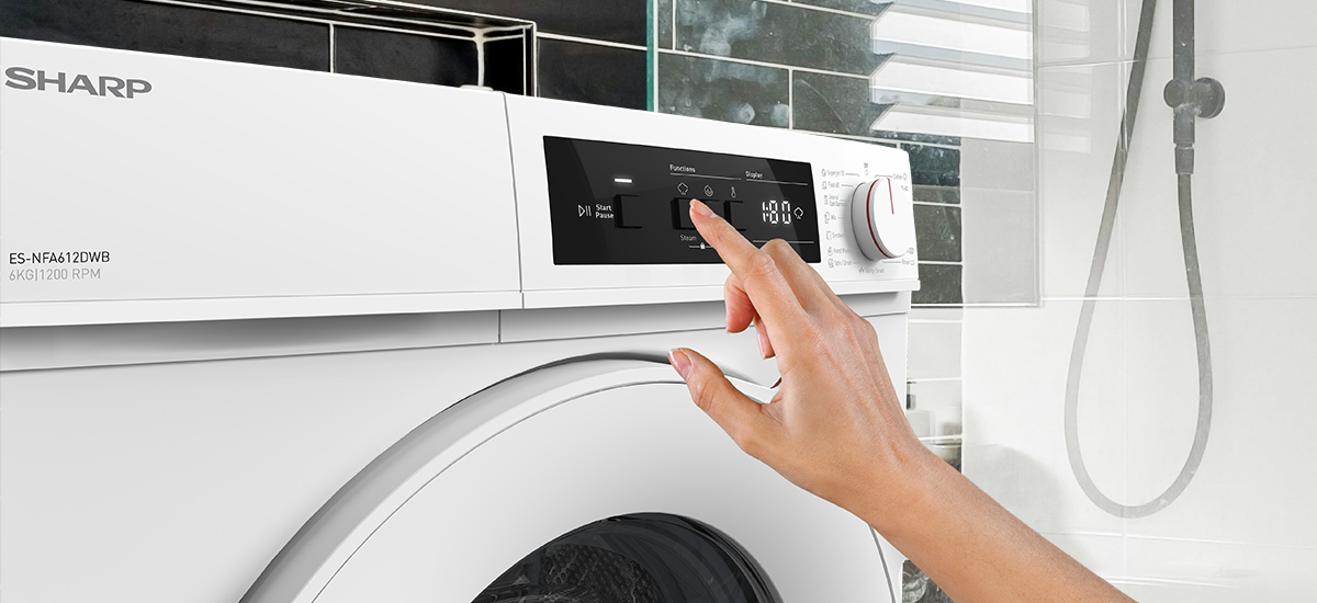 PRALKA SHARP ES-NFA612DWB-PL Na zdjęciu widać zbliżenie na panel sterowania białej pralki marki Sharp w łazience. Kobieca dłoń wybiera program na elektronicznym wyświetlaczu urządzenia. W tle widoczny jest fragment prysznica oraz połyskujące płytki ścienne funkcja pary czyste ubrania higiena odświeżanie włókna usuwanie bakterii alergeny zapachy zmiękczanie tkanin mniej zagnieceń łatwe prasowanie komfort alergicy dzieci pościel ręczniki bezpieczeństwo skóry