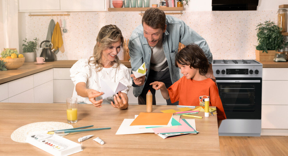 KUCHNIA GORENJE MEKS6141X lifestyle kuchnia rodzina dziecko akcesoria plastyczne na stole kuchenka w tle kolor czarno srebrny okap półki czajnik akcesoria kuchenne na blacie