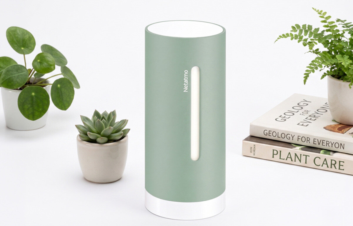 Moduł wewnętrzny NETATMO Original Nim-M Mint Moduł wewnętrzny Netatmo stoi na białym tle w otoczeniu małych sukulentów oraz książek o roślinach.