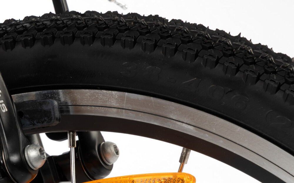Zbliżenie na oponę rowerową z widocznym bieżnikiem i fragmentem metalowej obręczy. Na oponie widoczny jest napis \'38-406\'.