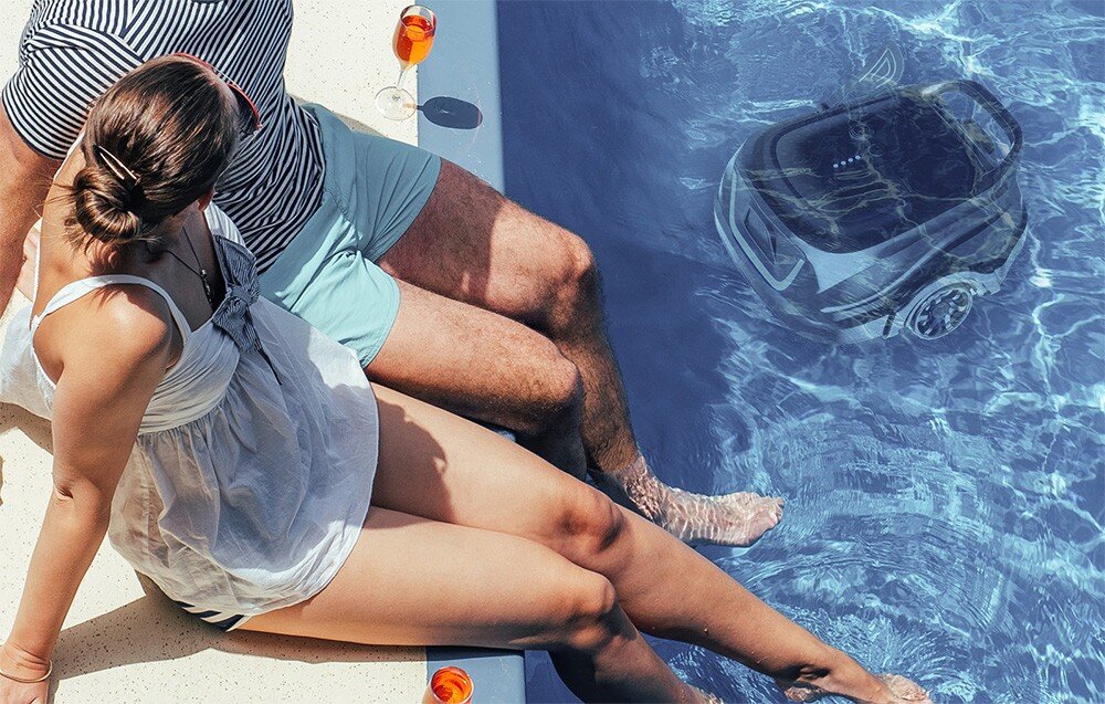 Robot do czyszczenia basenów WYBOT A1, woda, basen, czyszczenie, porządek, para siedzi na krawędzi basenu, na dnie basenu pracuje robot