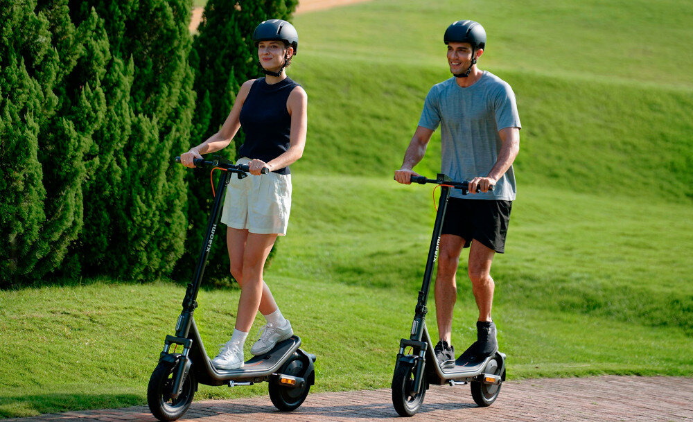 Hulajnoga elektryczna XIAOMI Electric Scooter 6 45km 400W 2 amortyzatory 12 cali Czarny park dwie osoby jadą na hulajnogach w tle trawnik mobilność środek codziennego transportu wygoda bezpieczeństwo