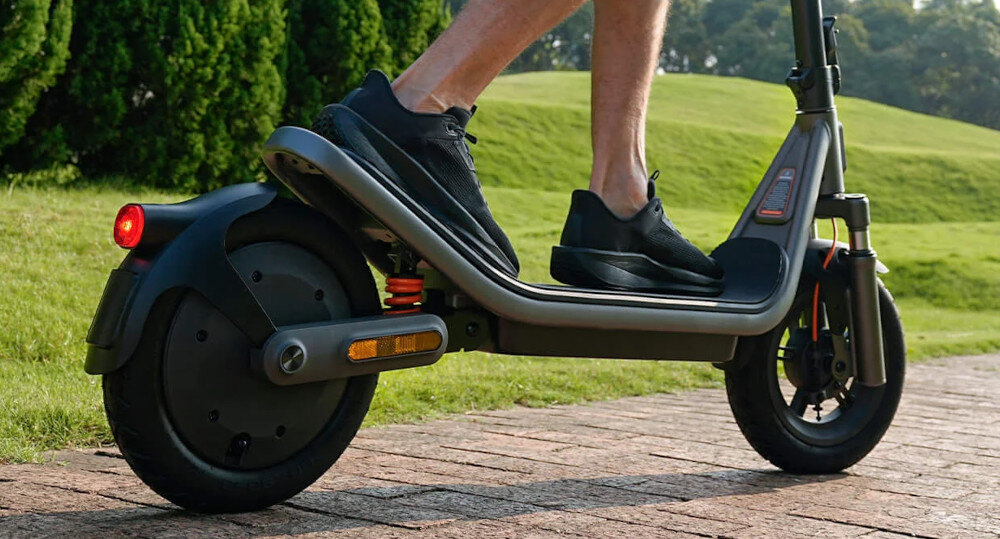 Hulajnoga elektryczna XIAOMI Electric Scooter 6 45km 400W 2 amortyzatory 12 cali Czarny park chodnik osoba jedzie na hulajnodze zbliżenie na podest w tle trawnik drzewa krzewy z wysokogatunkowej stali węglowej HC420 klasy samochodowej ponadprzeciętna sztywność i odporność na odkształcenia skutecznie tłumi drgania stabilność prowadzenia i bezpieczeństwo udźwig do 120 kg