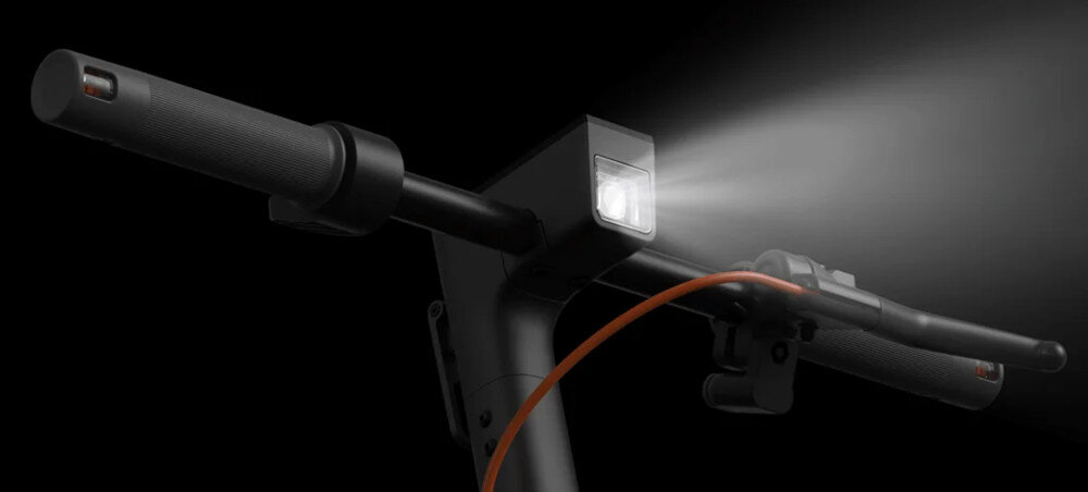Hulajnoga elektryczna XIAOMI Electric Scooter 6 45km 400W 2 amortyzatory 12 cali Czarny ciemne tło zbliżenie na przód kierownicy włączone przednie światło przednie światło o mocy 2,5 W bardzo dobra widoczność w ciemności (nawet do 15 metrów) wbudowane kierunkowskazy tylne światło stopu bezpieczeństwo