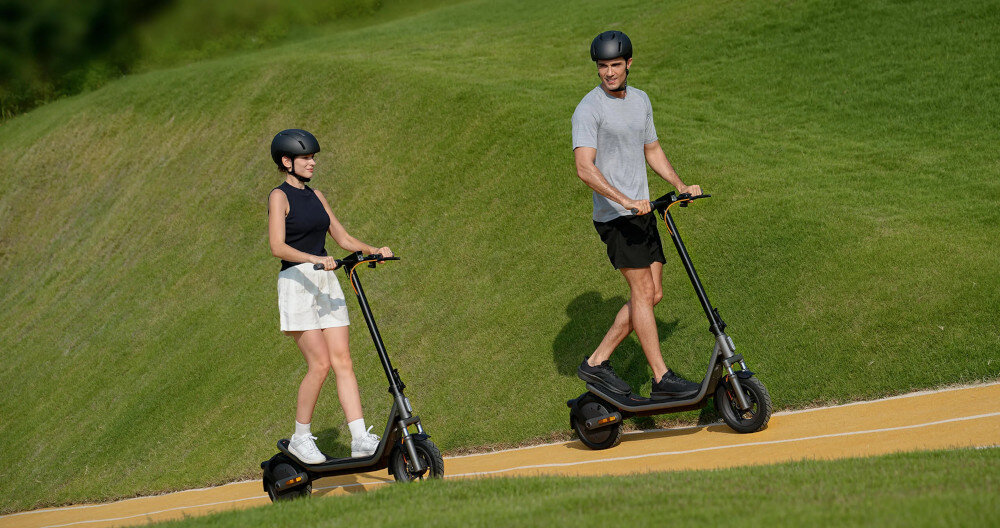 Hulajnoga elektryczna XIAOMI Electric Scooter 6 45km 400W 2 amortyzatory 12 cali Czarny park dwie osoby jadą na hulajnogach pod górkę w tle trawnik silnik o mocy 400 W cicha praca i płynna kontrola prędkości pokonuje wzniesienia o nachyleniu do 18% maksymalna prędkość do 20 km/h