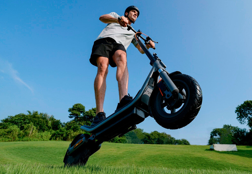 Hulajnoga elektryczna XIAOMI Electric Scooter 6 45km 400W 2 amortyzatory 12 cali Czarny park trawnik osoba jedzie na hulajnodze po trawniku przednie koło hulajnogi uniesione nad ziemią niebo 30 mm przednie zawieszenie z podwójnymi sprężynami i tylne z pojedynczą sprężyną profesjonalny system zawieszenia skutecznie tłumi wstrząsy