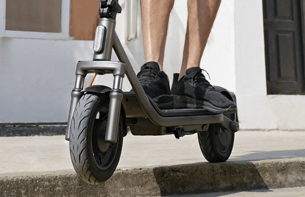 Hulajnoga elektryczna XIAOMI Electric Scooter 6 Lite Lite 25km 300W Amortyzacja 10 cali Czarny park chodnik osoba jedzie na hulajnodze zbliżenie na podest w tle budynek z wysokogatunkowej stali węglowej HC420 klasy samochodowej waga 18,1 kg ponadprzeciętna sztywność i odporność na odkształcenia skutecznie tłumi drgania stabilność prowadzenia i bezpieczeństwo udźwig do 100 kg