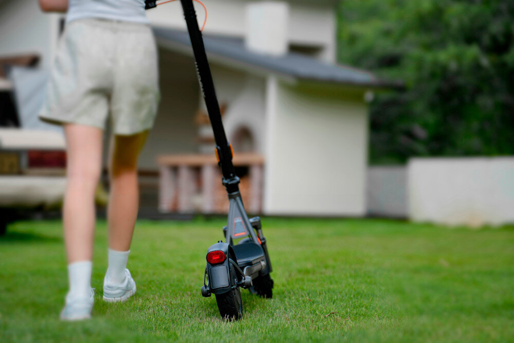 Hulajnoga elektryczna XIAOMI Electric Scooter 6 Lite Lite 25km 300W Amortyzacja 10 cali Czarny trawnik osoba prowadzi hulajnogę po trawniku w tle dom 3 tryby jazdy tryb PIESZY prędkość do 6 km/h tryb STANDARD prędkość do 15 km/h tryb SPORT prędkość do 20 km/h