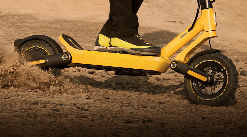 Hulajnoga elektryczna XIAOMI Electric Scooter 6 Ultra 75km 500W 2 Amortyzatory 12 cali Żółty piach osoba jedzie na hulajnodze po piasku terenowa konstrukcja podwozia pozwala swobodniej poruszać się po szutrze, kostce brukowej czy leśnych ścieżkach jazda w zróżnicowanym terenie staje się płynniejsza i bardziej komfortowa