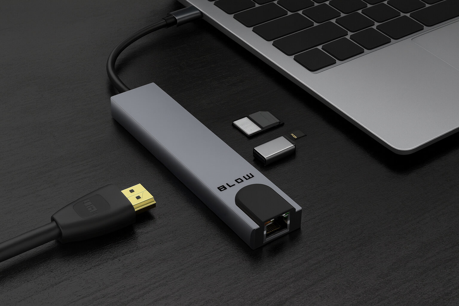 Na ciemnym biurku znajduje się srebrny rozgałęźnik z napisem \'BLOW\', podłączony do laptopa. Obok leżą trzy małe adaptery i kabel HDMI.