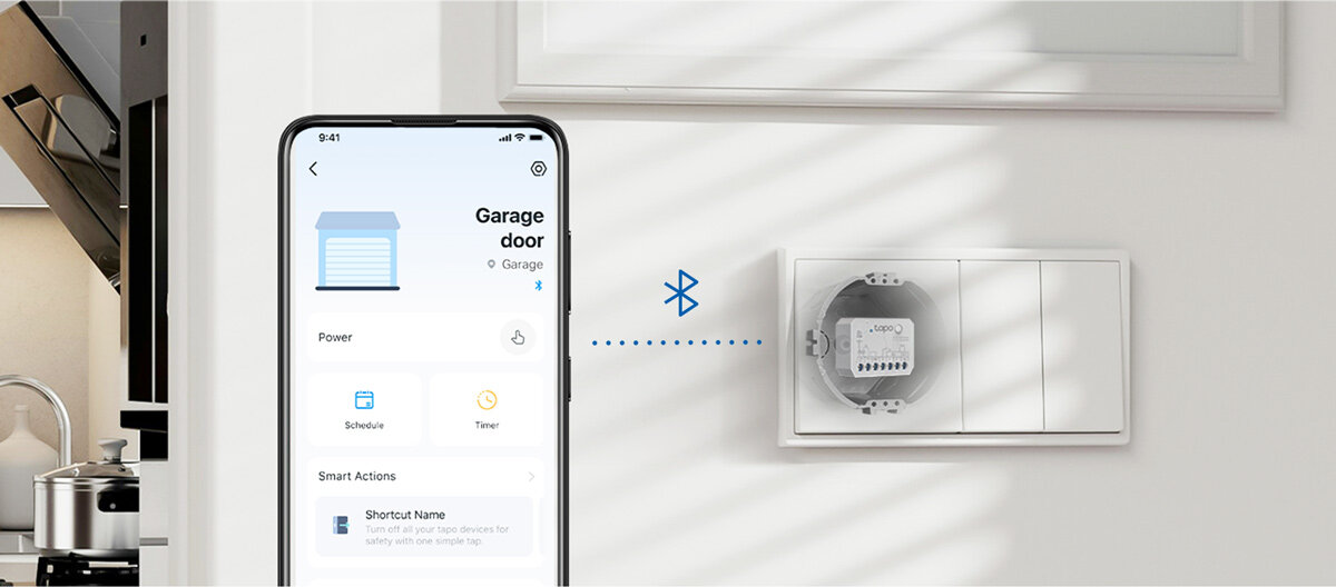 Obraz przedstawia smartfon z aplikacją do sterowania drzwiami garażowymi oraz inteligentny sterownik zamontowany na ścianie. Na ekranie telefonu widoczny jest tekst: \'Garage door\', \'Power\', \'Schedule\', \'Timer\', \'Smart Actions\', \'Shortcut Name\'.