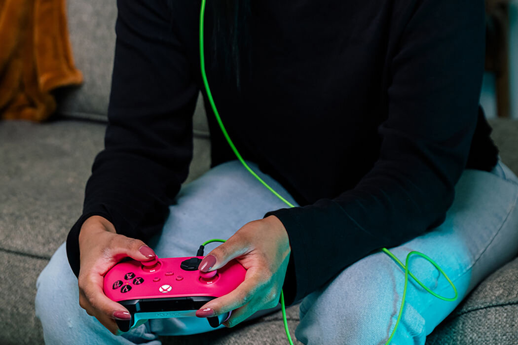 Osoba trzyma różowy kontroler do gier z widocznym logo Xbox. Kontroler jest podłączony zielonym kablem.