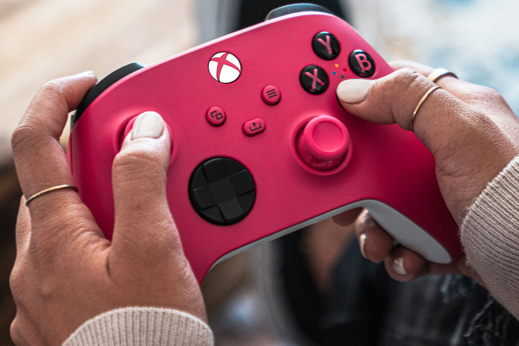 Osoba trzyma różowy kontroler do gier z widocznym logo Xbox. Na kontrolerze znajdują się przyciski oznaczone literami Y, B, A, X oraz krzyżak kierunkowy.