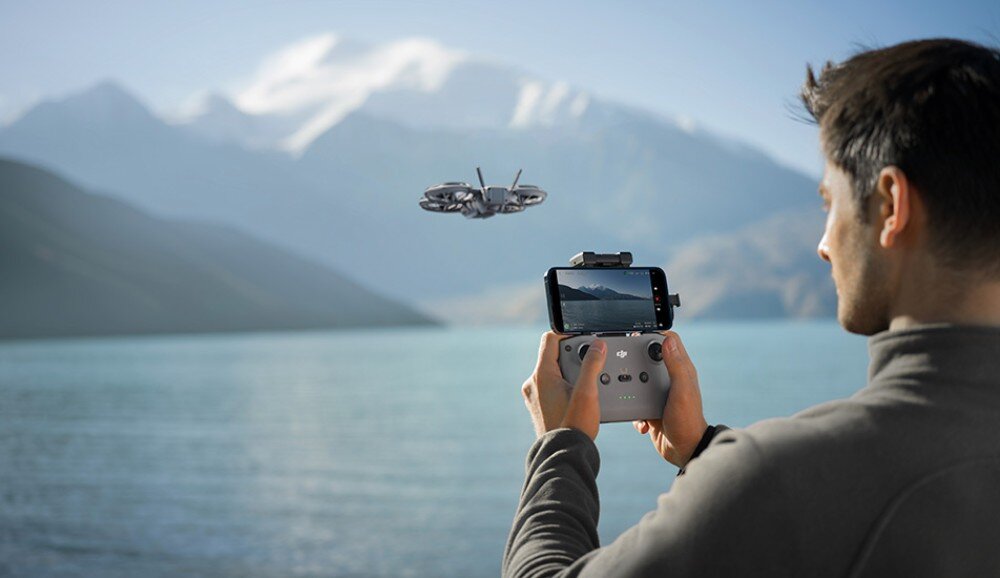 Dron DJI Neo 2 Motion Fly More Combo Mężczyzna w goglach i z kontrolerem jednoręcznym steruje małym dronem na tle nieba, warianty, gogle