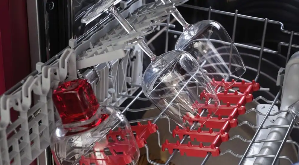 Wnętrze zmywarki z widocznymi kieliszkami umieszczonymi w specjalnych uchwytach. Uchwyt na kieliszki jest koloru czerwonego.