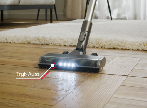 Odkurzacz z logo Amica na głowicy, wyposażony w rząd świateł LED, znajduje się na drewnianej podłodze. Obok widoczny jest napis \'Tryb Auto\'.