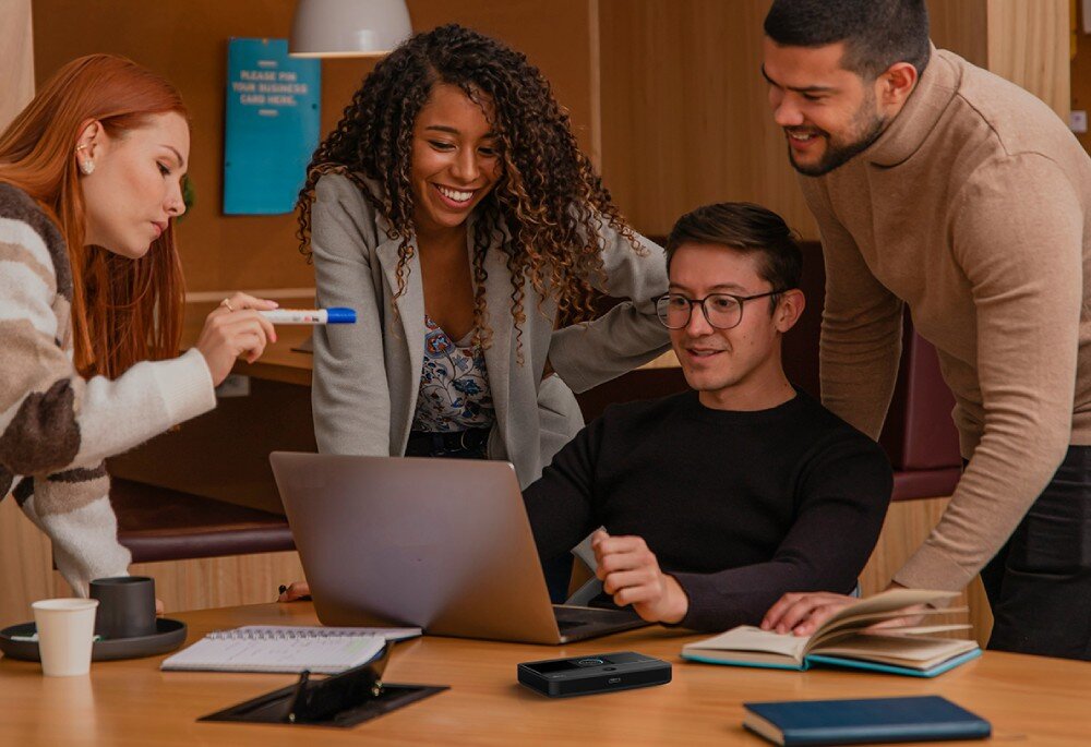 Router TP-LINK M7352 Grupa czterech osób pochylona nad laptopem przy biurku, na którym leży czarny hotspot mobilny