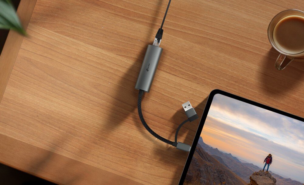 Karta sieciowa TP-LINK UE310C Szary, metalowy adapter sieciowy leżący na drewnianym blacie, połączony czarnym kablem w oplocie do tabletu oraz kablem sieciowym z wtykiem RJ-45