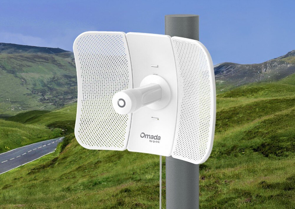 Most bezprzewodowy TP-LINK Omada Beam Bridge 5 UR Kit biały bezprzewodowy most zamontowany na metalowym słupie na tle górzystego krajobrazu z drogą asfaltową