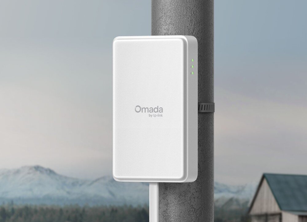 Router TP-LINK Omada ER701-5G-Outdoor Białe prostokątne urządzenie z napisem Omada zamontowane pionowo na szarym słupie za pomocą metalowej opaski na tle zamglonych gór