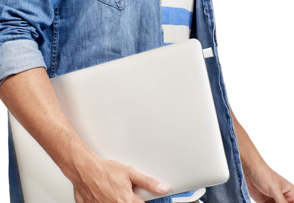 Karta sieciowa MERCUSYS MA60XNB Mężczyzna w dżinsowej koszuli trzyma pod pachą zamknięty srebrny laptop z wpiętym w boczny port małym białym adapterem USB