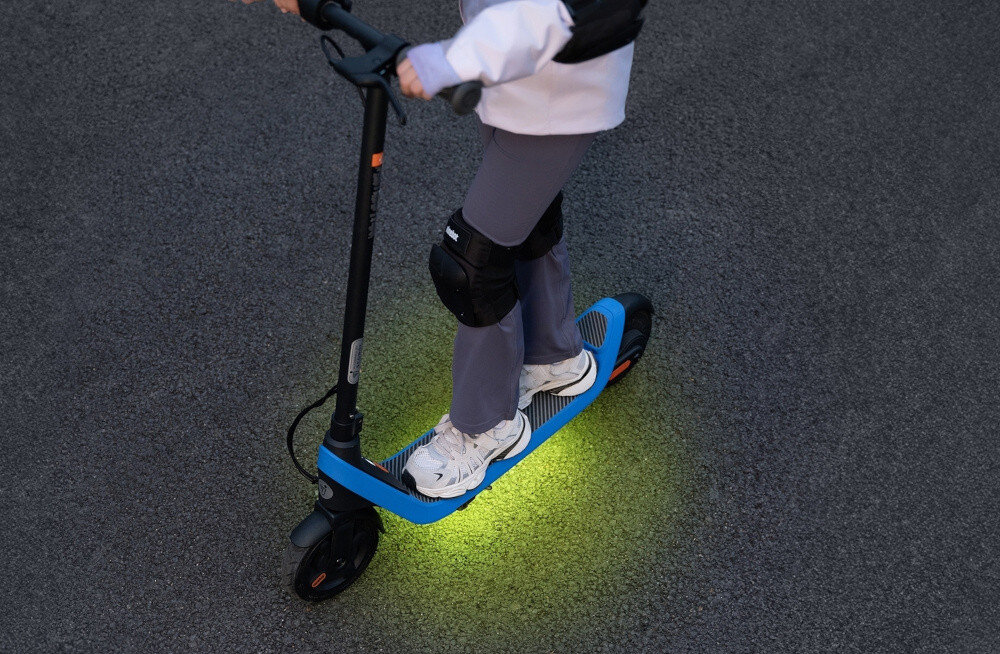 Hulajnoga elektryczna SEGWAY Ninebot C2 Lite 9km 130W 7 cali Czarno-niebieski droga chodnik widok z góry dziecko jedzie na hulajnodze widoczne podświetlone podwieszenie podświetlane zawieszenie z ponad 250 kolorami i systemem oświetlenia RGB synchronizuje się z wybranym trybem jazdy dynamiczne światła zwiększają widoczność pojazdu w ciemności poprawiają bezpieczeństwo