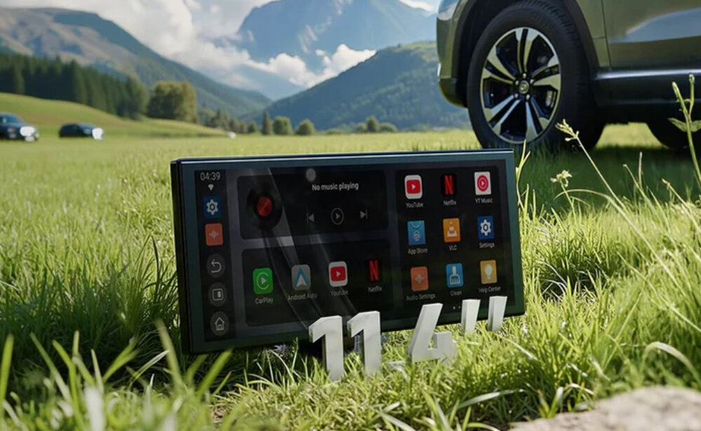Tablet z ekranem dotykowym o przekątnej 11,4 cala stoi na trawie, wyświetlając różne aplikacje, takie jak YouTube, Netflix i Spotify. W tle widoczne są góry i samochód.