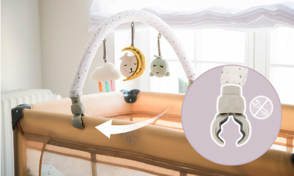 Pałąk z zabawkami przymocowany do łóżeczka, z wiszącymi pluszowymi zabawkami w kształcie chmurki, księżyca i gwiazdki. Obok znajduje się powiększenie klipsa mocującego z symbolem narzędzi.