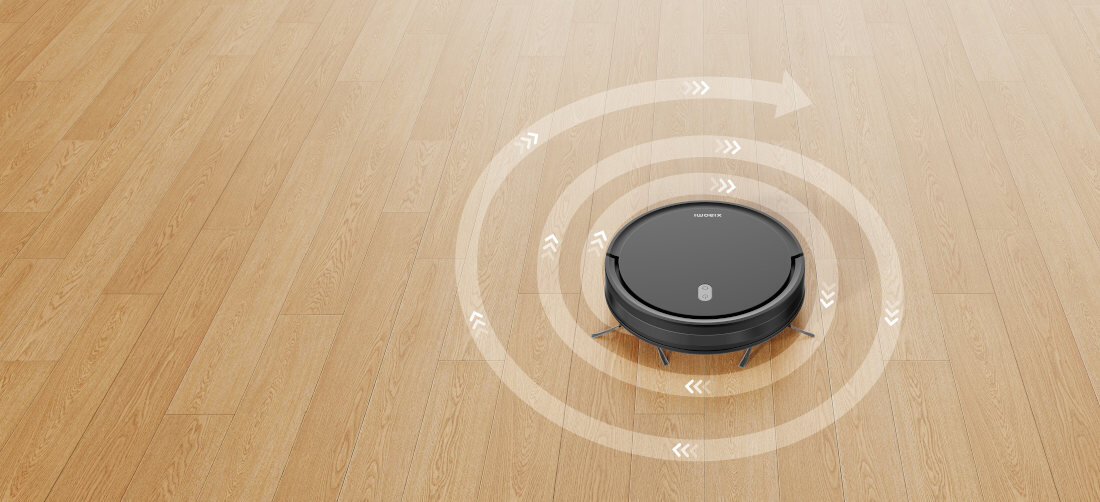 Czarny robot sprzątający porusza się po drewnianej podłodze, wokół niego widoczne są strzałki wskazujące kierunek ruchu. Na robocie widoczne jest logo \'XIAOMI\'.
