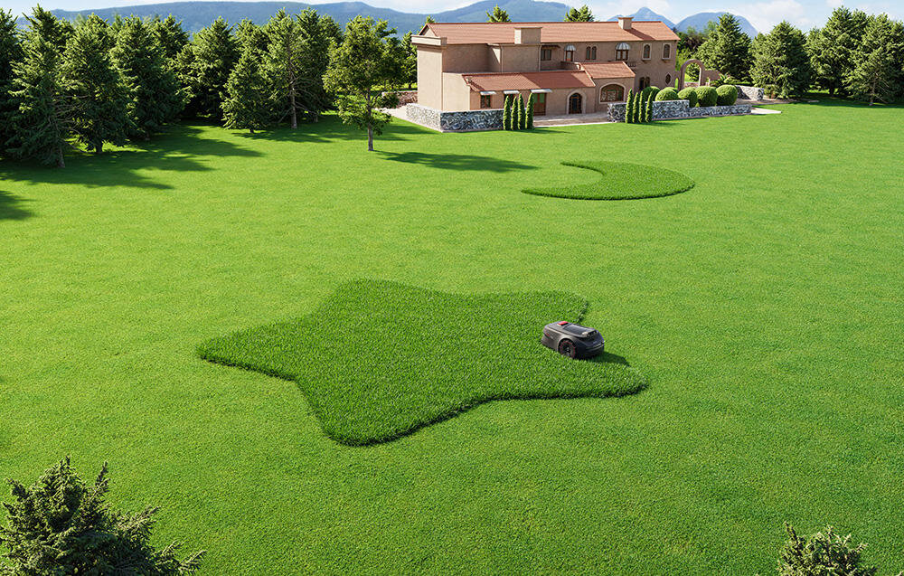 Na dużym, zielonym trawniku znajduje się robot koszący, który kosi trawę w kształcie gwiazdy. W tle widoczny jest duży dom otoczony drzewami.
