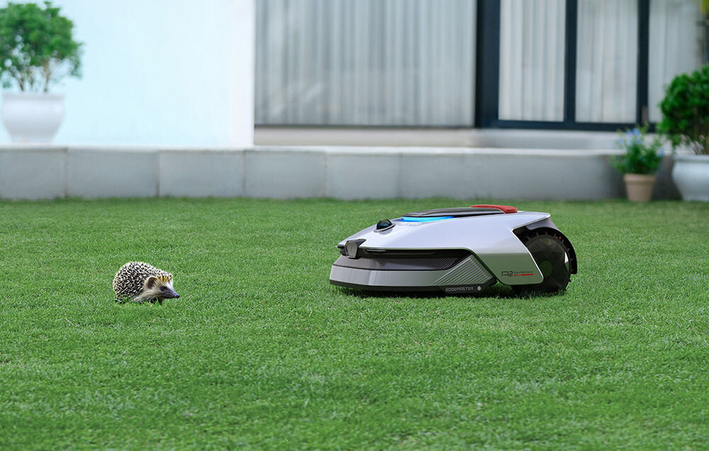 Robot koszący DREAME A2 1200 ogród trawnik robot kosi trawę przed robotem stoi jeż w tle dom przełomowy system OmniSense™ 2.0 zaawansowany układ czujników 3D wspierany kamerą HDR i algorytmami AI LiDAR 3D o zasięgu wykrywania do 70 metrów szerokim kącie widzenia 360° x 59° centymetrowej precyzji kamera 1080p HDR z funkcjami sztucznej inteligencji analizuje otoczenie w czasie rzeczywistym szczegółowa, trójwymiarowa mapa terenu