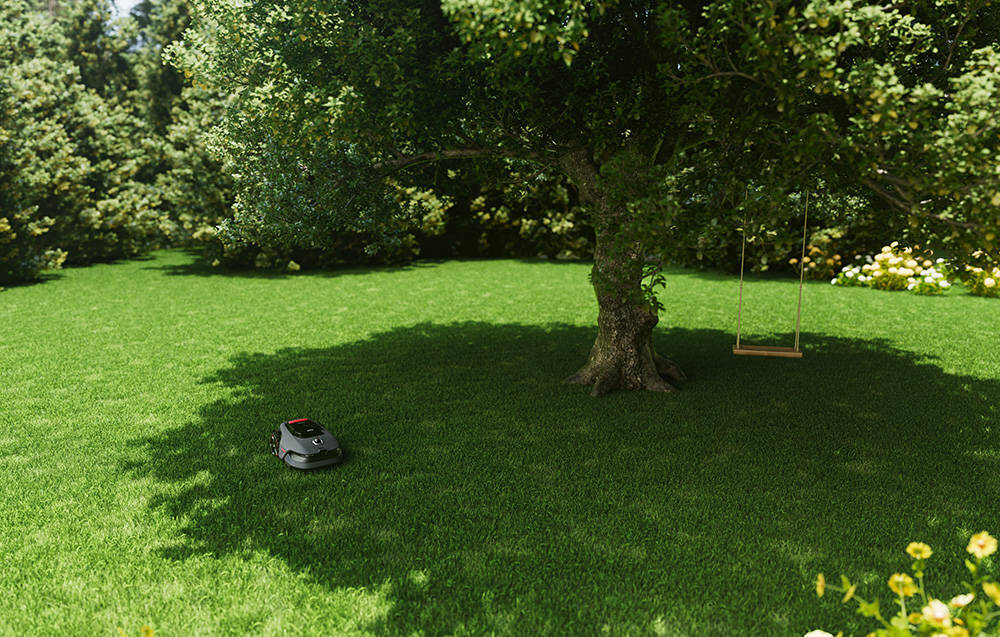 Na trawniku w ogrodzie znajduje się robot koszący, obok dużego drzewa z huśtawką. W tle widoczne są krzewy i kwiaty.