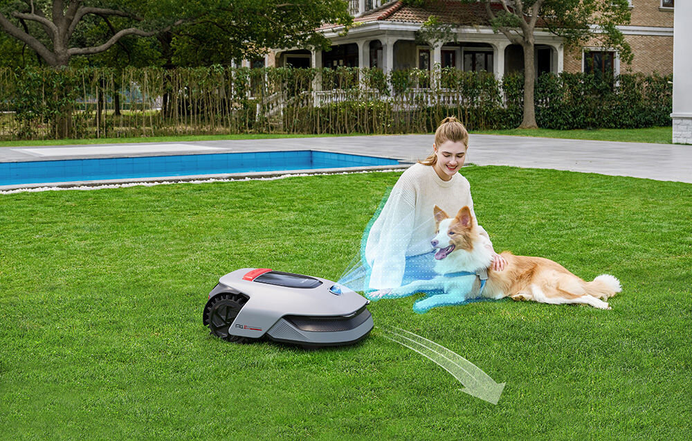 Robot koszący DREAME A1 PRO 1000 ogród trawnik robot kosi trawę na trawniku siedzi osoba z psem w tle dom basen zaawansowany system wielokierunkowego unikania przeszkód danych punktów 3D w chmurze inteligentnych algorytmach rozpoznaje przeszkody i płynnie je omija bezpieczeństwo