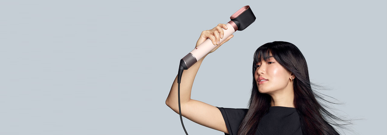 Modelka z ciemnymi włosami podsusza włosy używając multistylera Dyson Airwrap Coanda2x z końcówką do wstępnego podsuszania.