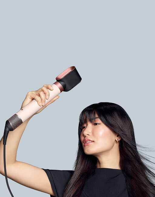 Modelka z ciemnymi włosami podsusza włosy używając multistylera Dyson Airwrap Coanda2x z końcówką do wstępnego podsuszania. Wersja mobile.