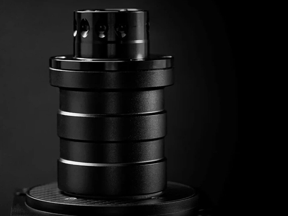 Baza kierownicy SIMAGIC Alpha 15 Nm Direct Drive S102 Zbliżenie na metalowy wał bazy kierownicy z widocznymi pierścieniami konstrukcyjnymi, przedstawiony od boku na ciemnym tle