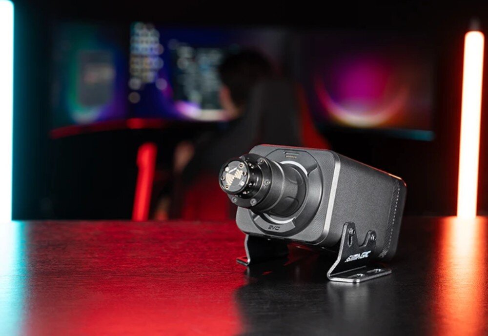 Baza kierownicy SIMAGIC Alpha Evo Pro 18 Nm S106 Czarna baza kierownicy z systemem szybkiego montażu stoi na metalowych wspornikach. W tle widać rozmytego gracza przed monitorami