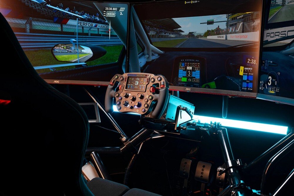 Symulator wyścigowy z kierownicą i trzema monitorami wyświetlającymi grę wyścigową. Na ekranach widoczny jest tor wyścigowy oraz interfejs gry.