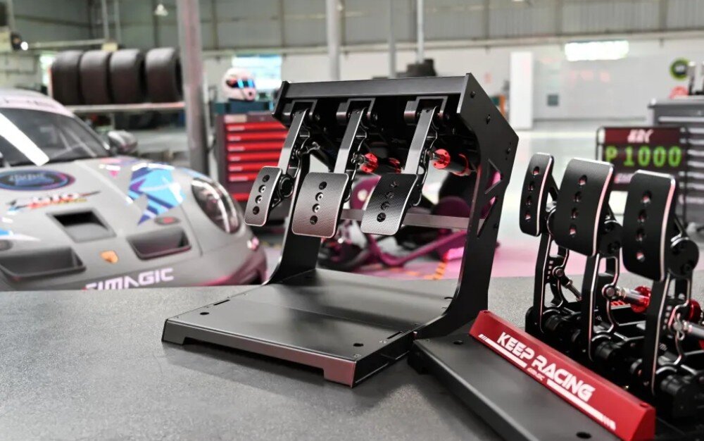 Zestaw SIMAGIC P1000i S304 Metalowy zestaw trzech pedałów simracingowych na podstawie, z napisem 'KEEP RACING', w tle samochód wyścigowy