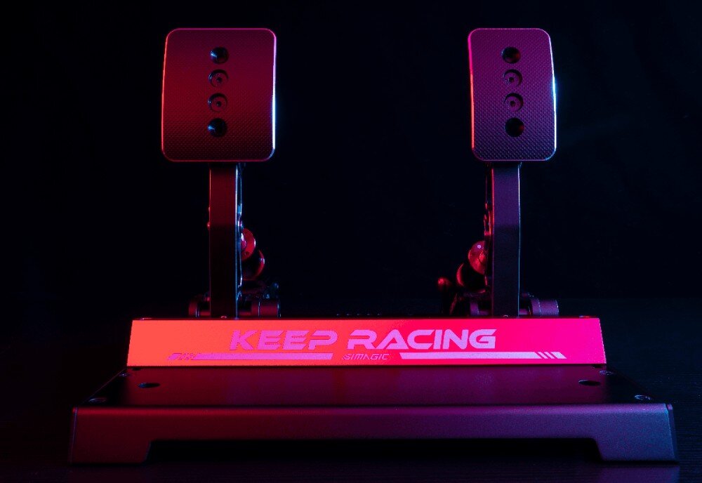 Na obrazie widoczne są dwa pedały symulatora wyścigowego z napisem \'KEEP RACING SIMAGIC\' na podstawie. Oświetlenie jest w kolorach czerwonym i niebieskim.