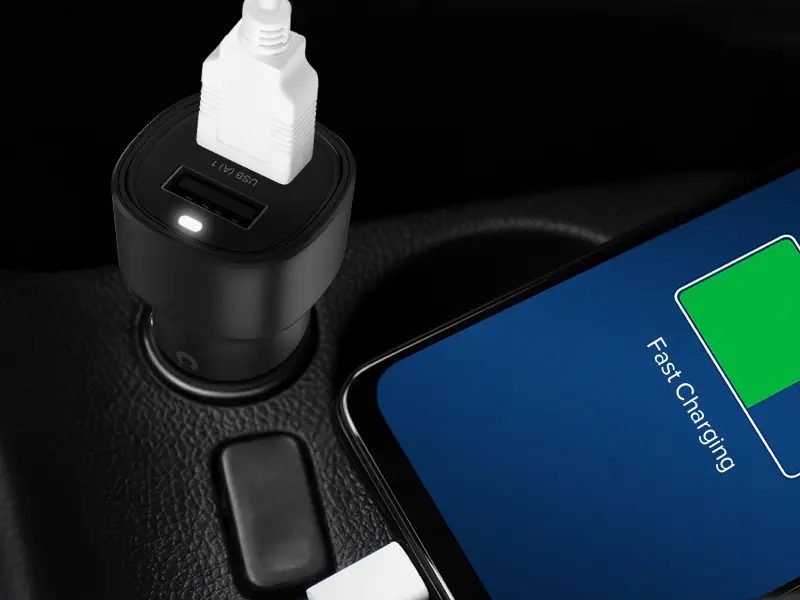 Czarna ładowarka samochodowa z dwoma portami USB-A, z jednym podłączonym białym kablem. Obok znajduje się telefon z wyświetlaczem pokazującym \'Fast Charging\'.