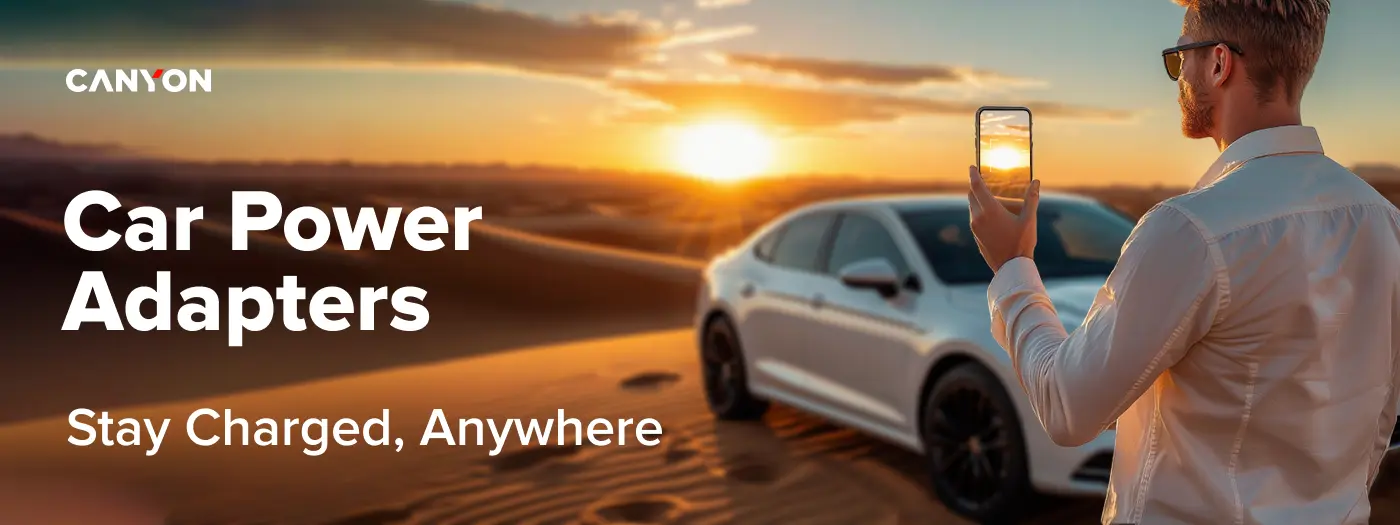 Na obrazie widoczny jest mężczyzna trzymający smartfon, stojący obok białego samochodu na pustyni o zachodzie słońca. Tekst na obrazie: \'CANYON Car Power Adapters Stay Charged, Anywhere\'.